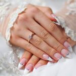 Bride holding bouquet with elegant oval nude wedding nails glistening in sunlight.
