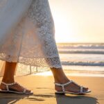 Bride wearing elegant white flat sandals with pearl embellishments walking on sandy beach during outdoor wedding ceremony